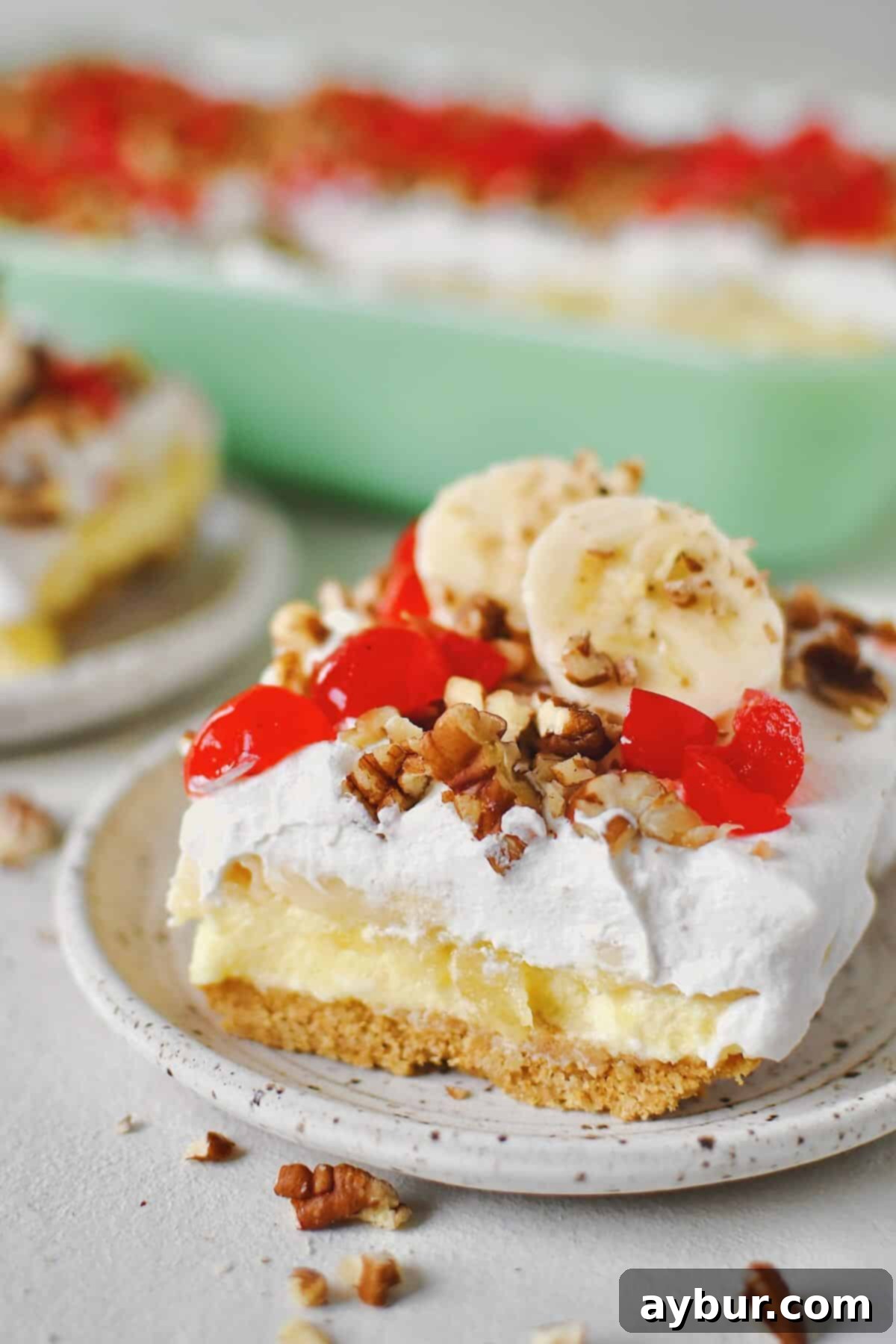 Ultimate Banana Split Cake 11 Several slices of Banana Split Cake, beautifully plated and ready to eat, topped with fresh banana slices and a sprinkle of pecans, alongside the remaining cake in the baking dish.