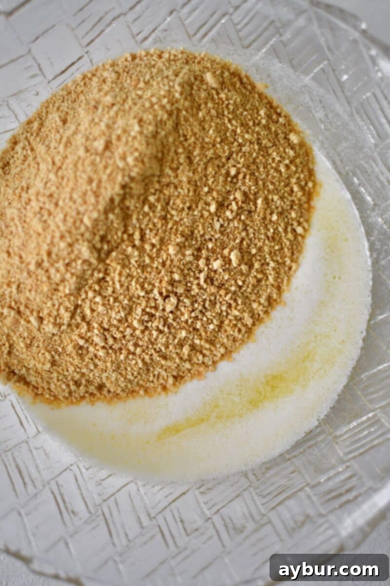 Ultimate Banana Split Cake 4 Melted butter combined with graham cracker crumbs in a mixing bowl, ready to be pressed into the baking dish for the crust.