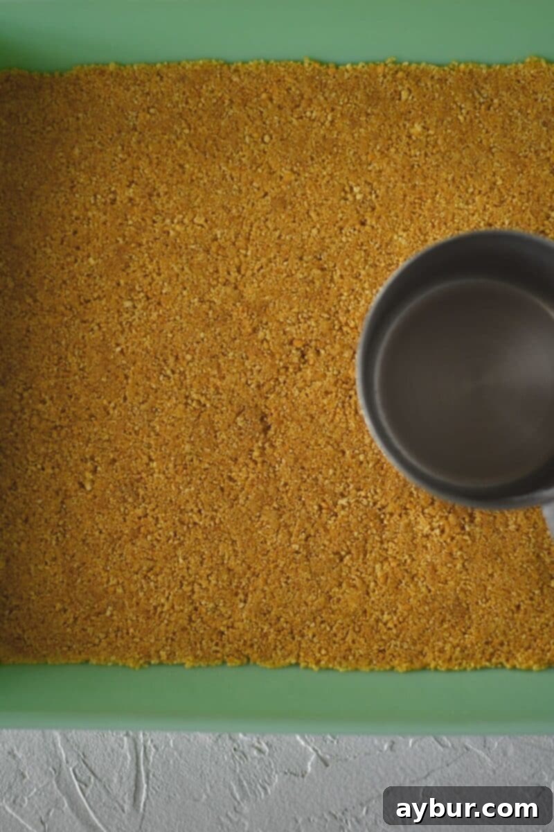 Ultimate Banana Split Cake 5 Firmly pressing the prepared graham cracker crust mixture into a 9x13 inch baking pan, ensuring an even and compact base for the cake.