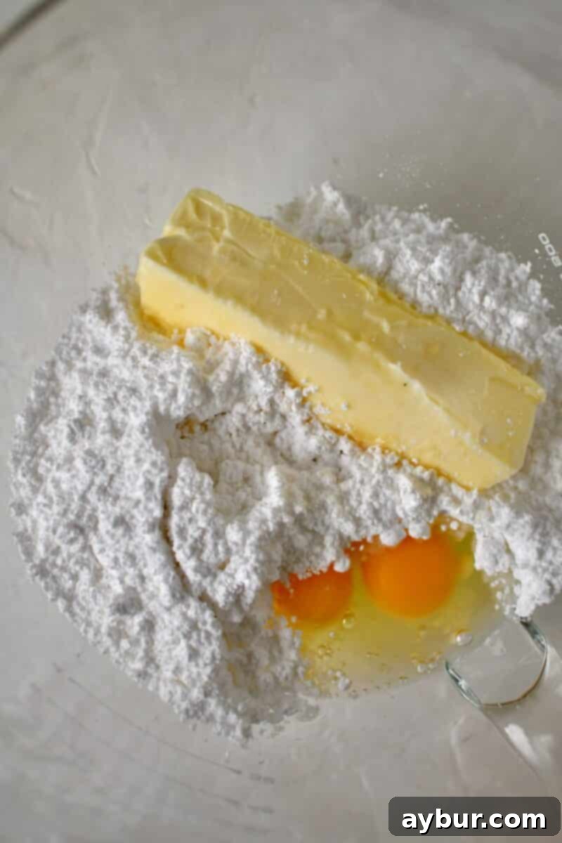 Ultimate Banana Split Cake 6 The process of making the creamy, fluffy filling in a stand mixer, combining butter, powdered sugar, vanilla, and eggs, to be spread over the graham cracker crust.