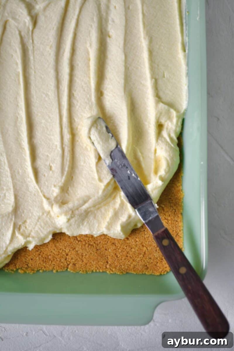 Ultimate Banana Split Cake 8 Carefully spreading the whipped, creamy filling evenly over the completely cooled graham cracker crust in the baking pan, forming the base of the cake.