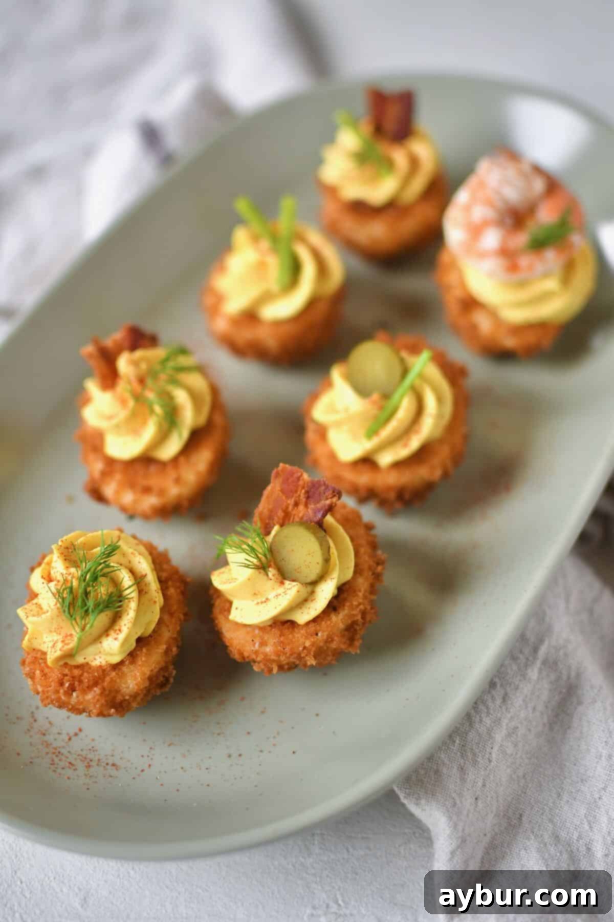 A platter of golden-brown Deep-Fried Deviled Eggs, generously topped with an exciting array of optional garnishes including sliced gherkins, fresh herbs like chives and dill, crispy bacon bits, and succulent sautéed shrimp, ready to be served as a unique appetizer.
