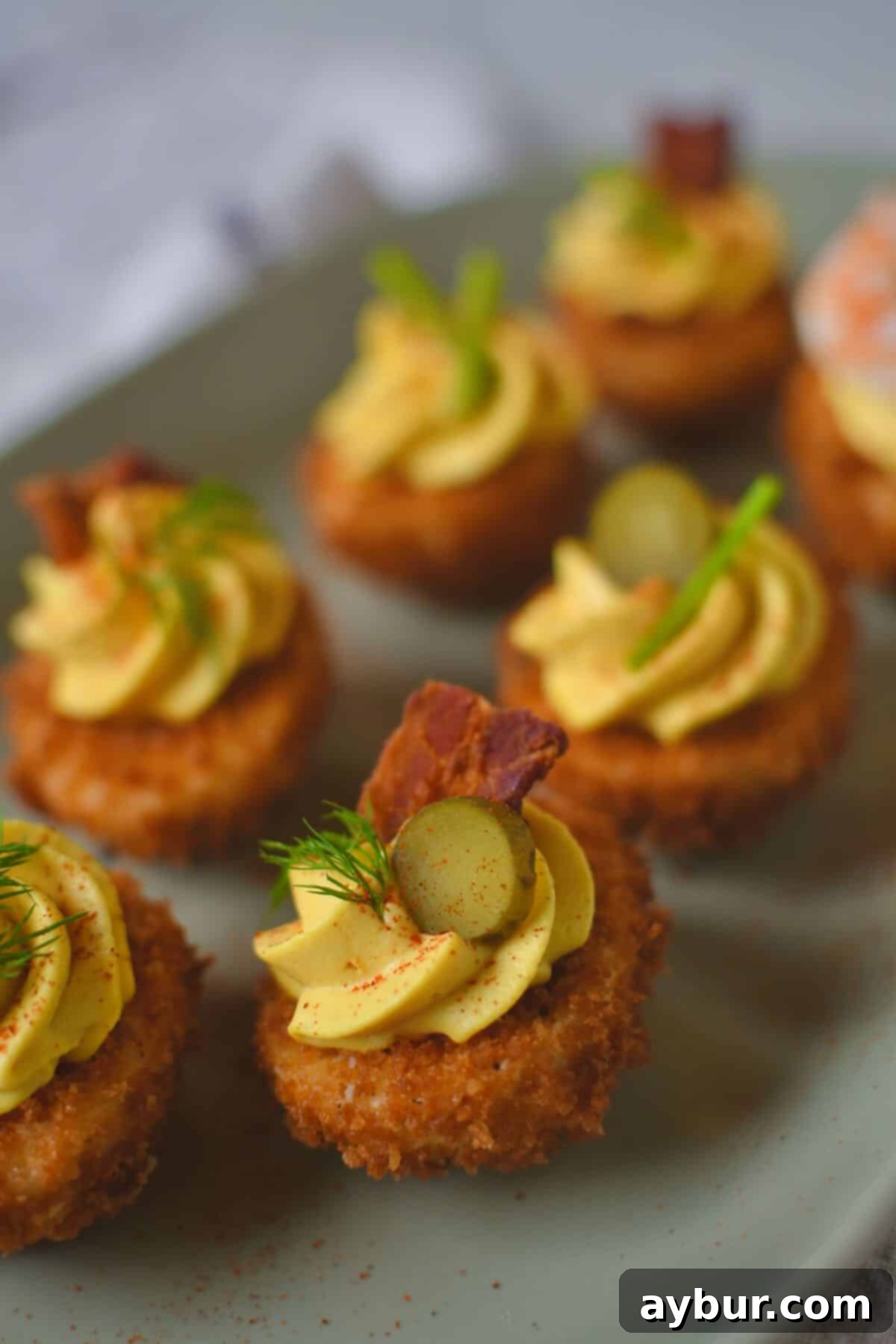 An enticing close-up of finished Deep-Fried Deviled Eggs, arranged on a rustic wooden board, showcasing their beautiful golden crust and creamy filling, adorned with a variety of fresh and savory toppings like crispy bacon, fresh chives, and tangy gherkin slices.