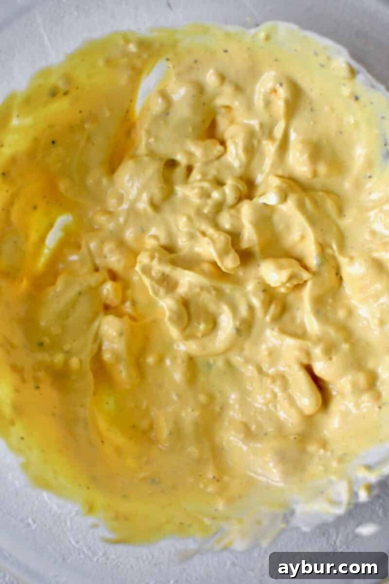 A close-up shot of egg yolk filling being meticulously mashed and blended in a small bowl with a fork, achieving a smooth and creamy consistency essential for perfect deviled eggs.