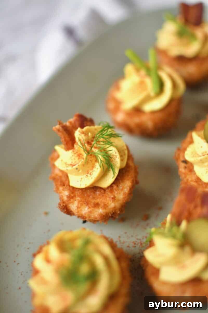A close-up of a single Deep-Fried Deviled Egg, showcasing its perfectly golden and crispy panko coating, generously filled with creamy yolk mixture and topped with a sprig of fresh dill, ready to be enjoyed as a gourmet bite.