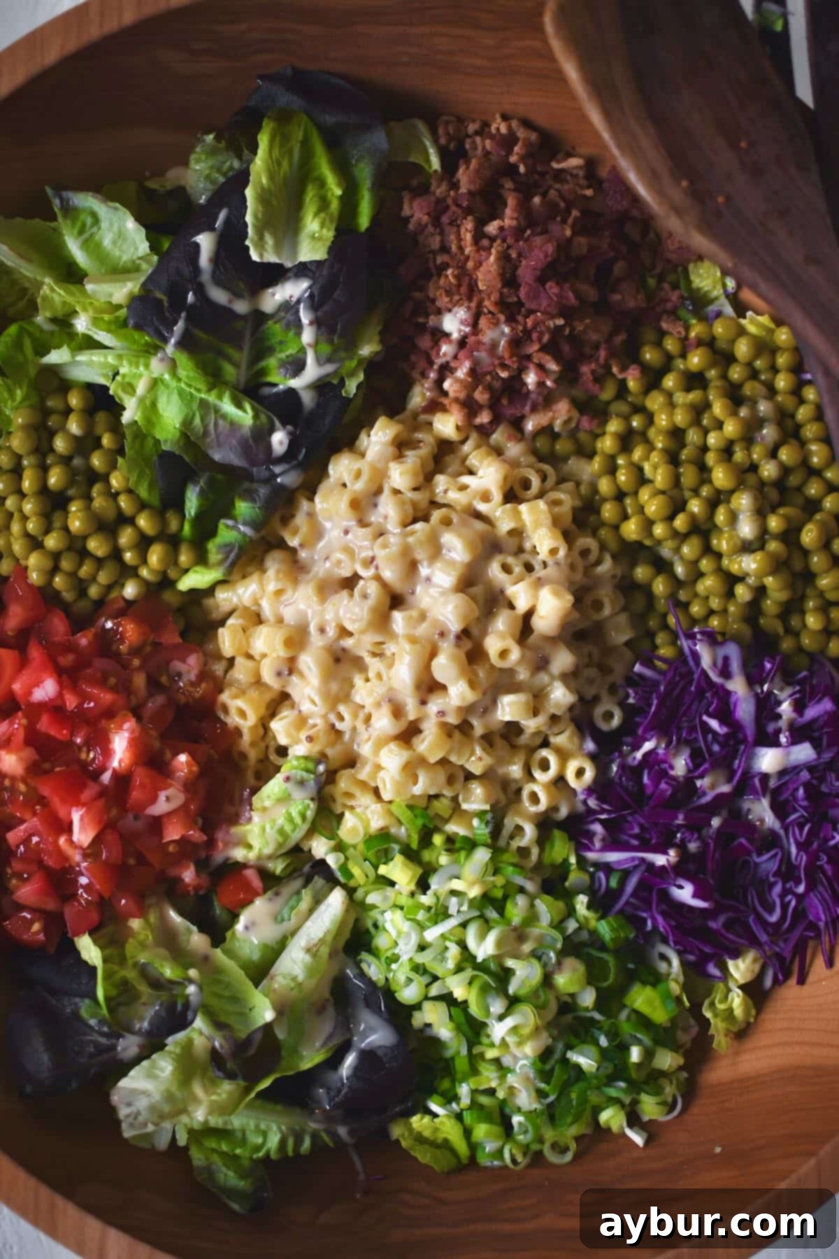 A vibrant Italian Pasta Salad, with chopped greens, pasta, tomatoes, bacon, and peas, ready to be tossed.