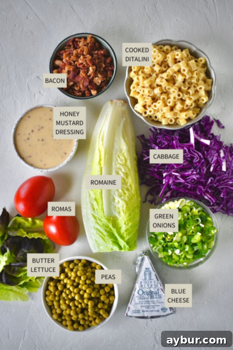 A flat lay of fresh ingredients for Italian Pasta Salad, including romaine, cabbage, butter lettuce, tomatoes, peas, bacon, and blue cheese.