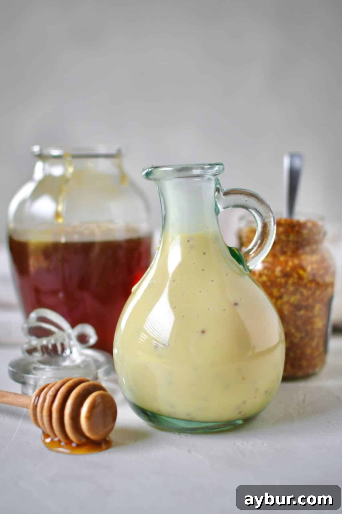 Zesty Honey Mustard Dressing 2 Dressing mixed up and placed in a storage bottle for later use. A honey jar and mustard jar sit behind it with a dripping honey dipper in front.