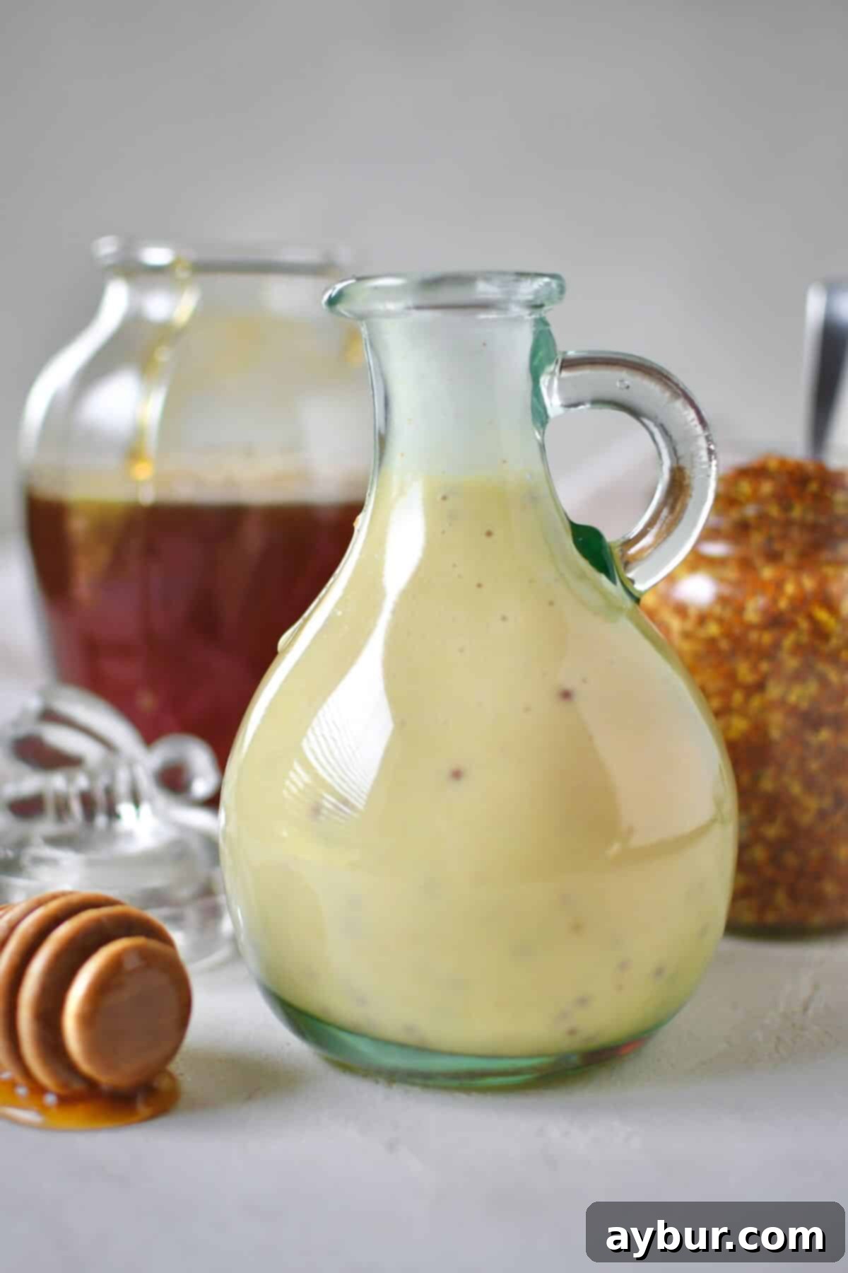 Zesty Honey Mustard Dressing 7 Dressing mixed up and placed in a storage bottle for later use. A honey jar and mustard jar sit behind it with a dripping honey dipper in front.
