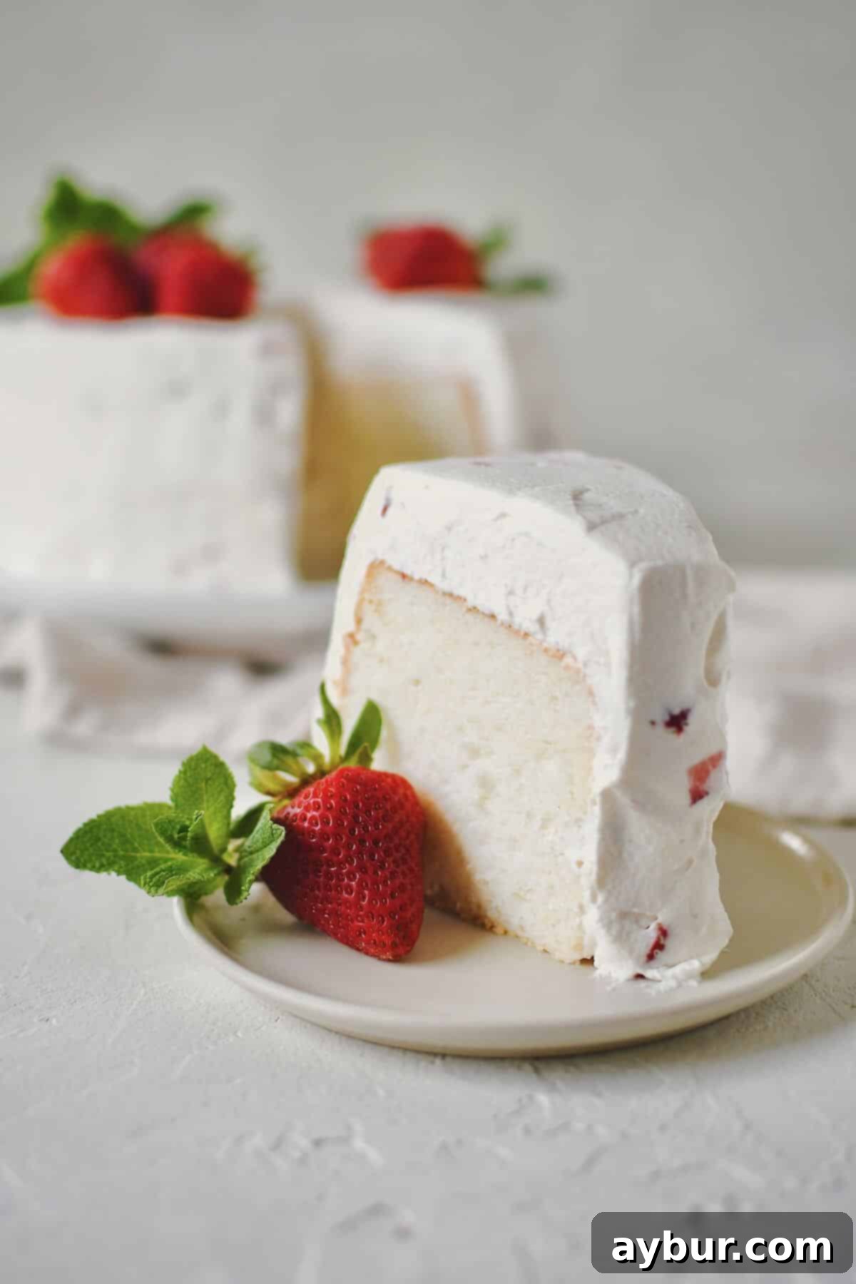 A beautifully frosted Strawberry Angel Food Cake with a slice removed, revealing its airy texture.
