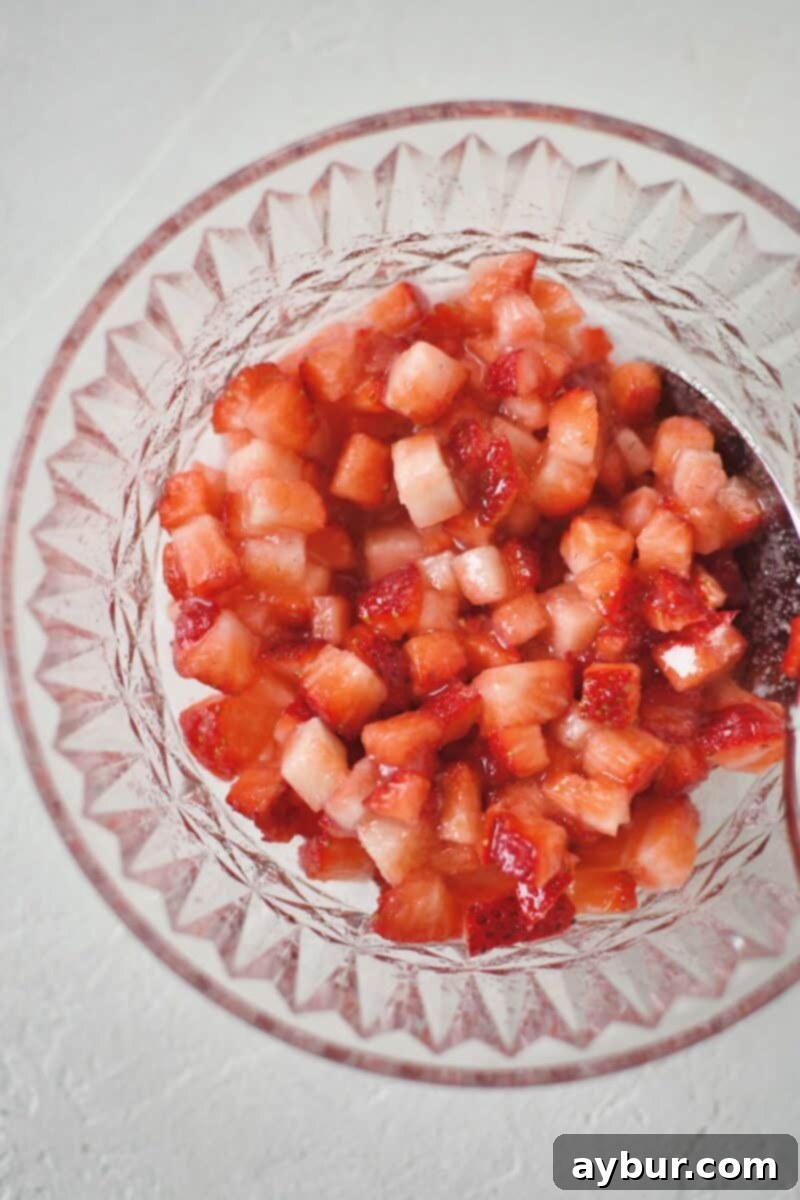 Diced strawberries and sugar mixed together in a bowl, beginning to macerate.