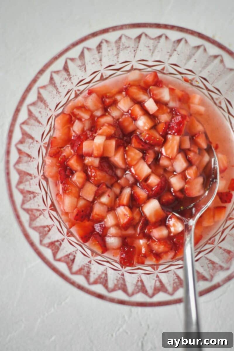Diced strawberries and sugar mixed together in a bowl, having sat long enough for juices to leach out, creating a syrup.