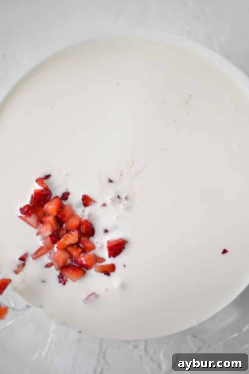 Heavy cream and macerated strawberries in the bowl of a stand mixer, before whipping, showing a liquid state.