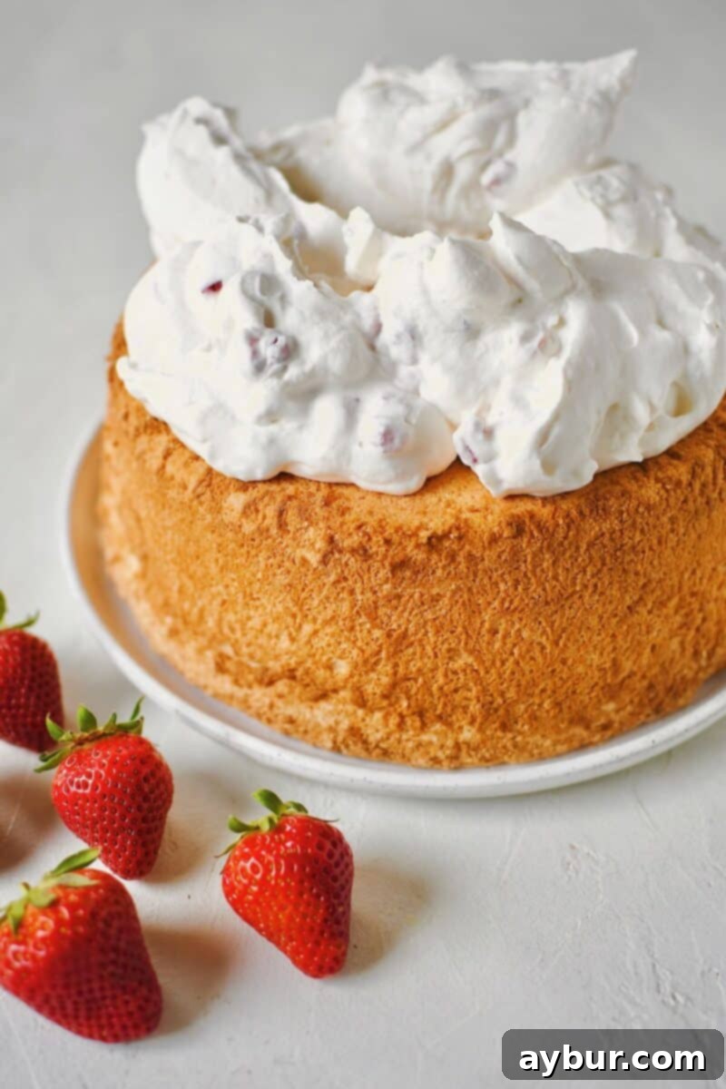 Strawberry whipped cream being scooped onto a cooled angel food cake.