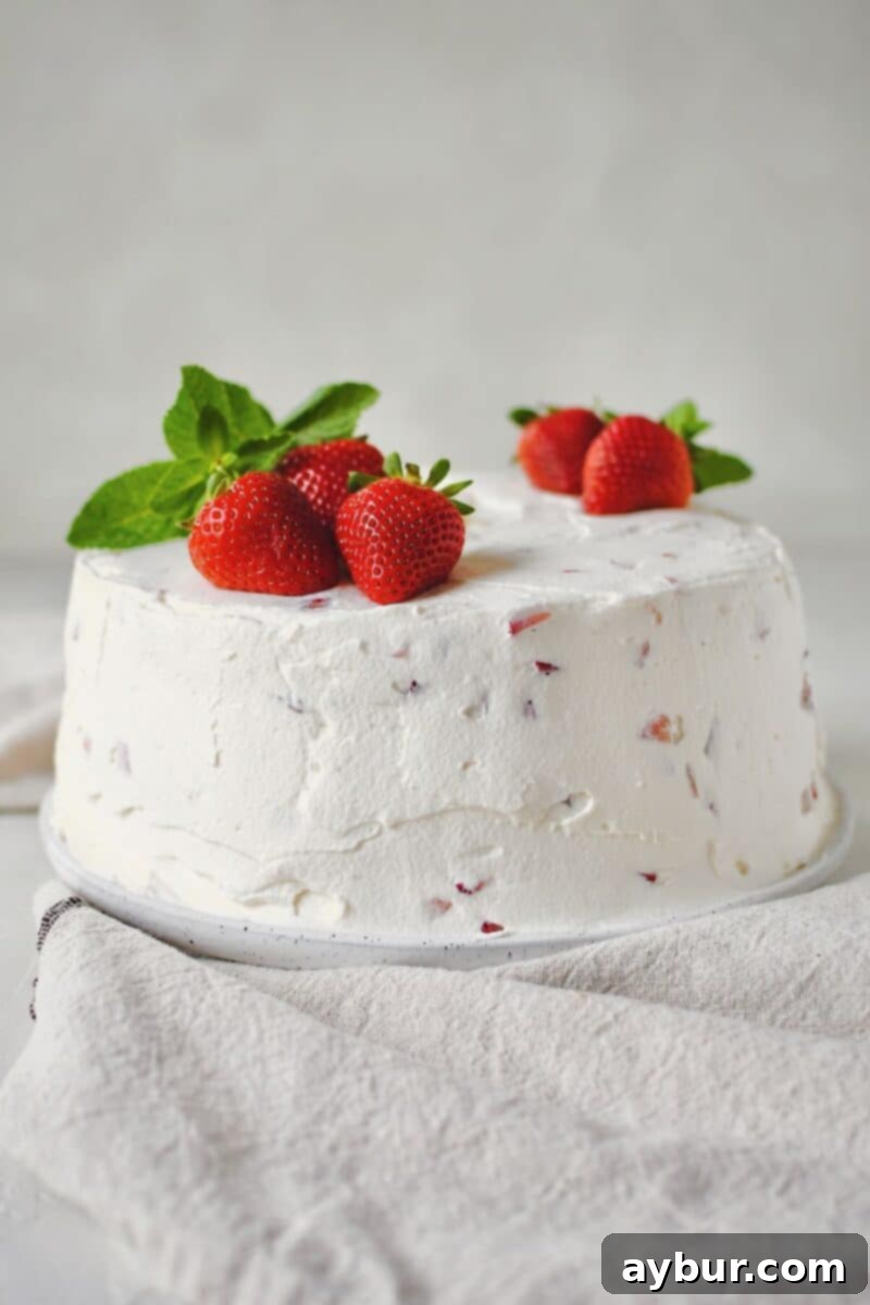 Strawberry Angel Food Cake freshly frosted, topped with whole strawberries and fresh mint leaves for garnish.