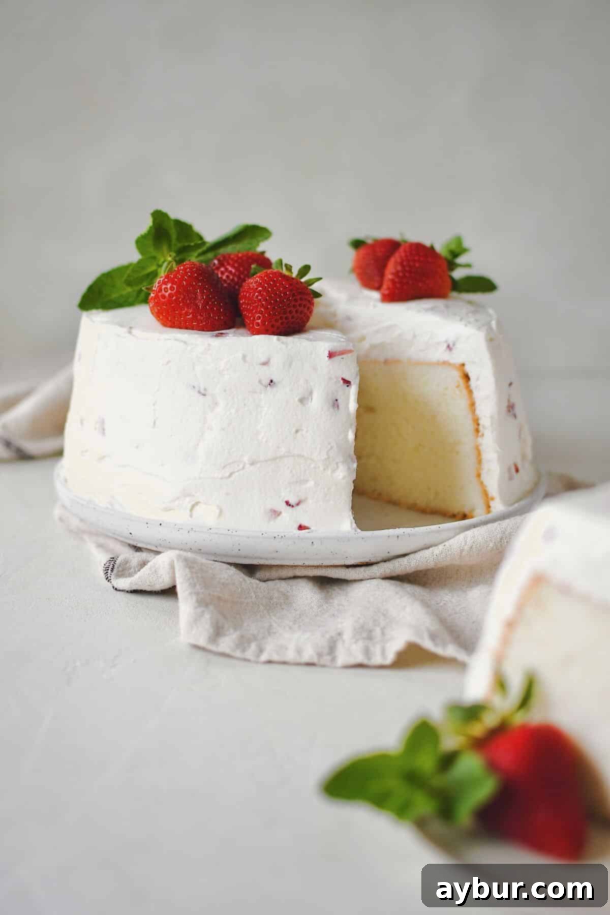 A slice of Strawberry Angel Food Cake has been cut, showing the soft interior and creamy topping.