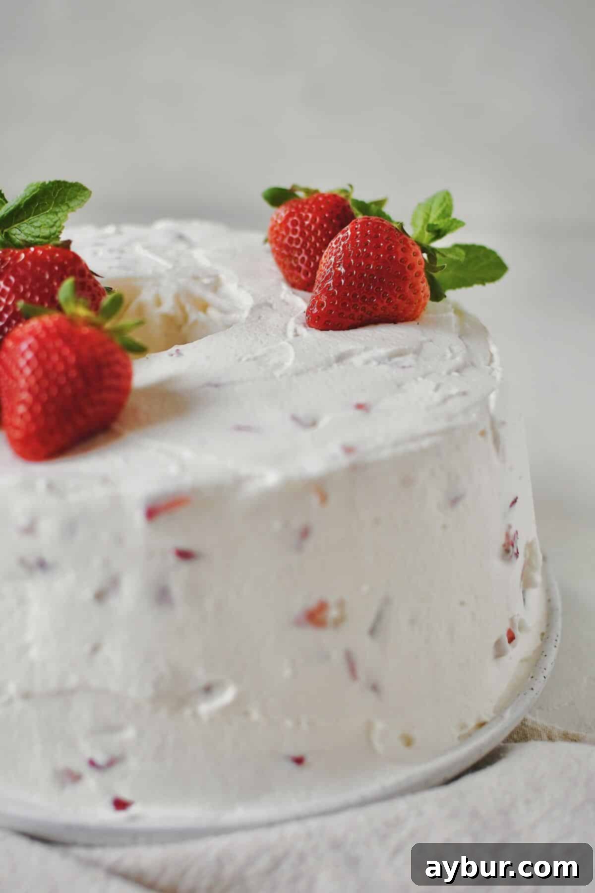 A beautifully frosted Strawberry Angel Food Cake topped with fresh whole strawberries and mint, ready to be served.