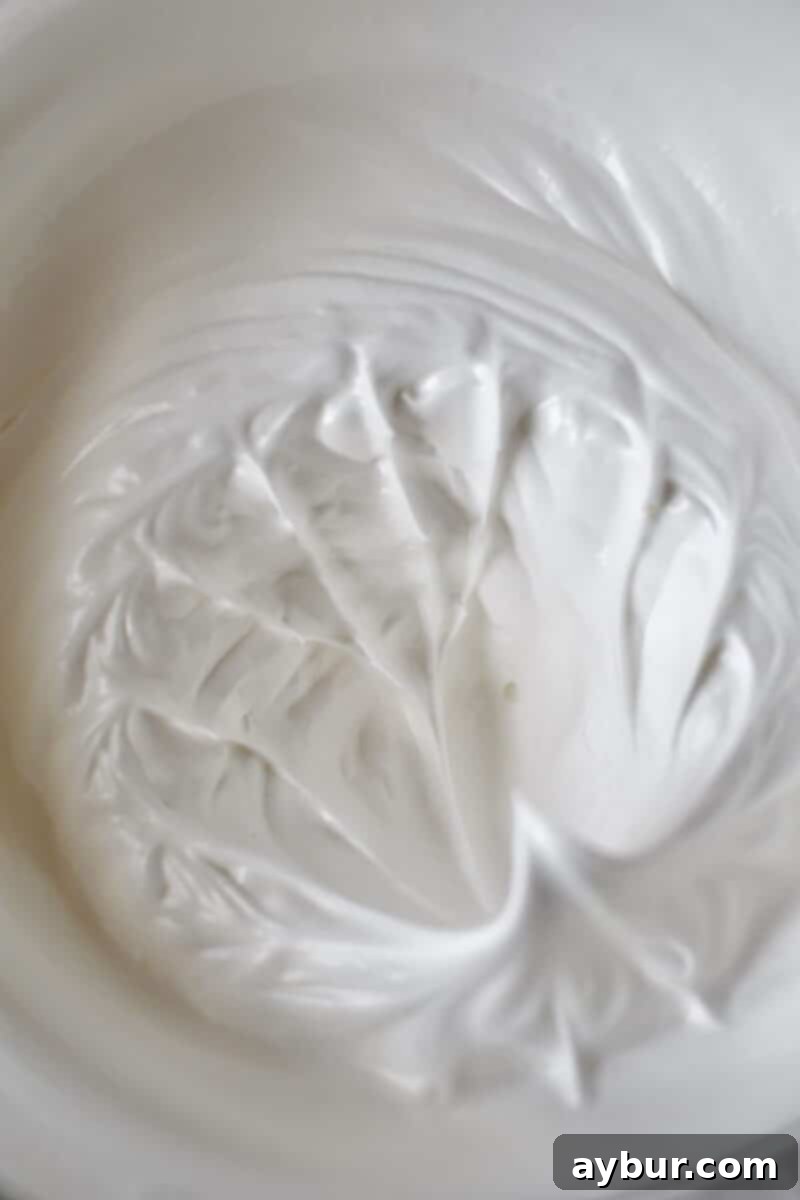 Perfectly whipped egg whites in a stand mixer bowl, forming stiff peaks.