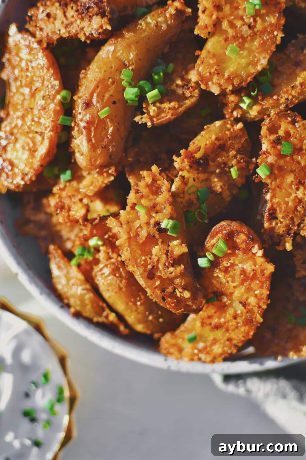 Parmesan Crusted Potatoes that have baked and cooled, in a serving bowl with a side of chive sour cream.