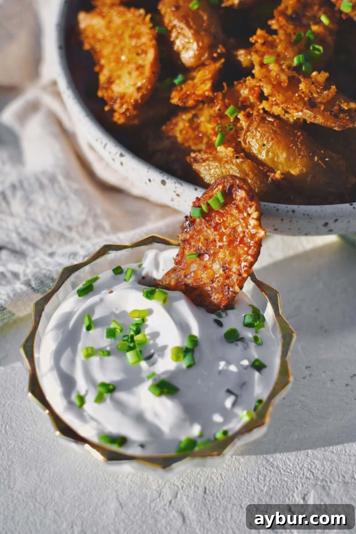 Parmesan Crusted Potatoes in a bowl with one being dipped in chive sour cream.