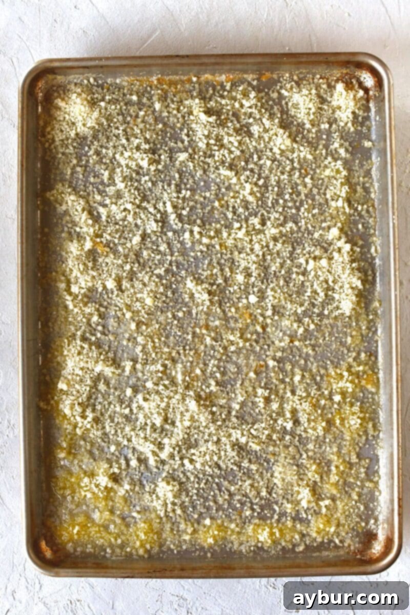 Grated parmesan cheese dusted over melted butter on a rimmed baking sheet.