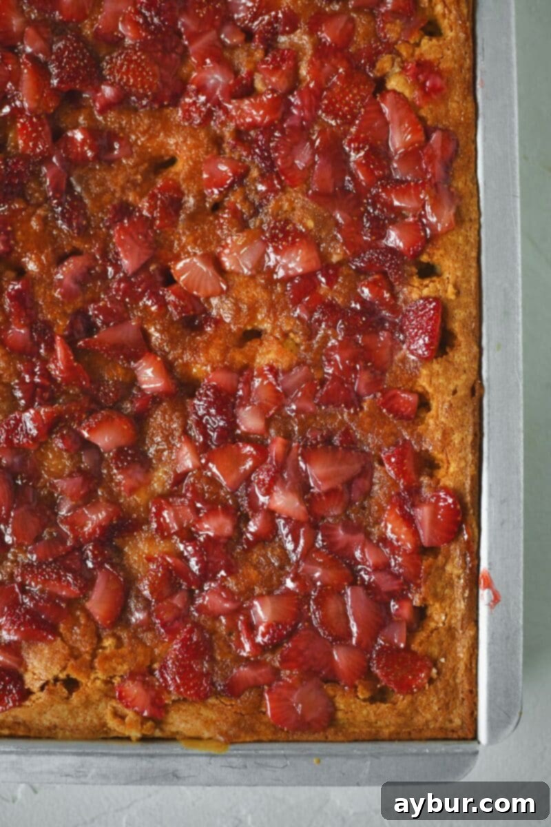 Spreading the cooked fresh strawberries over the poked cake.