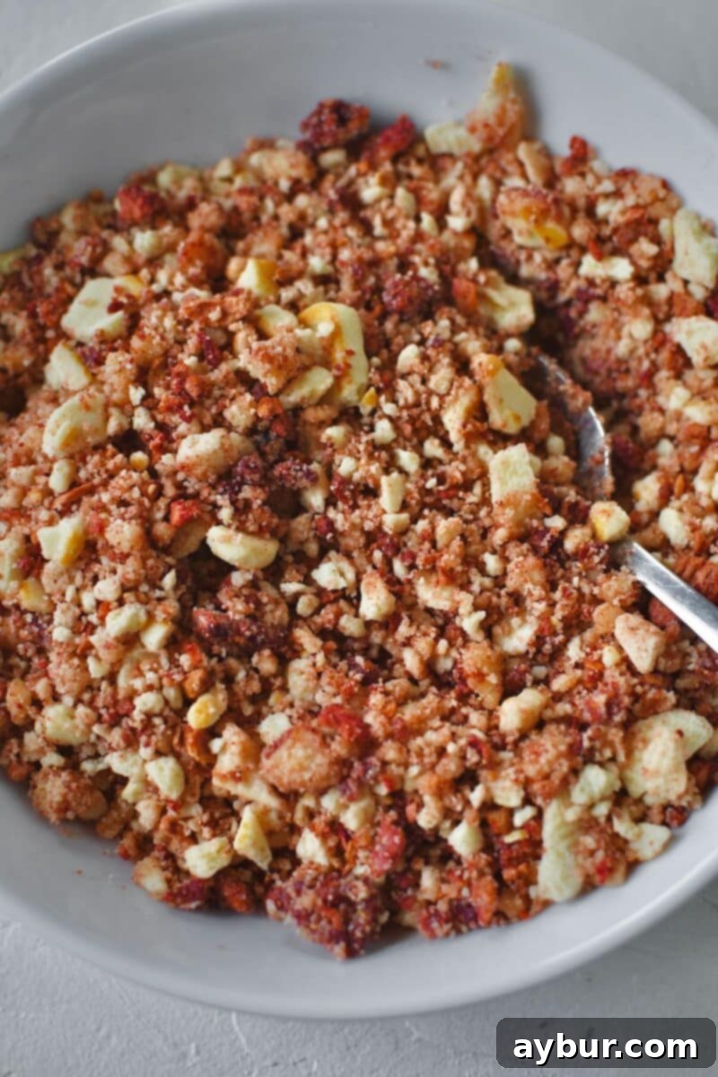 Crushed butter cookies and freeze dried strawberries in a bowl with butter added, after mixing together.