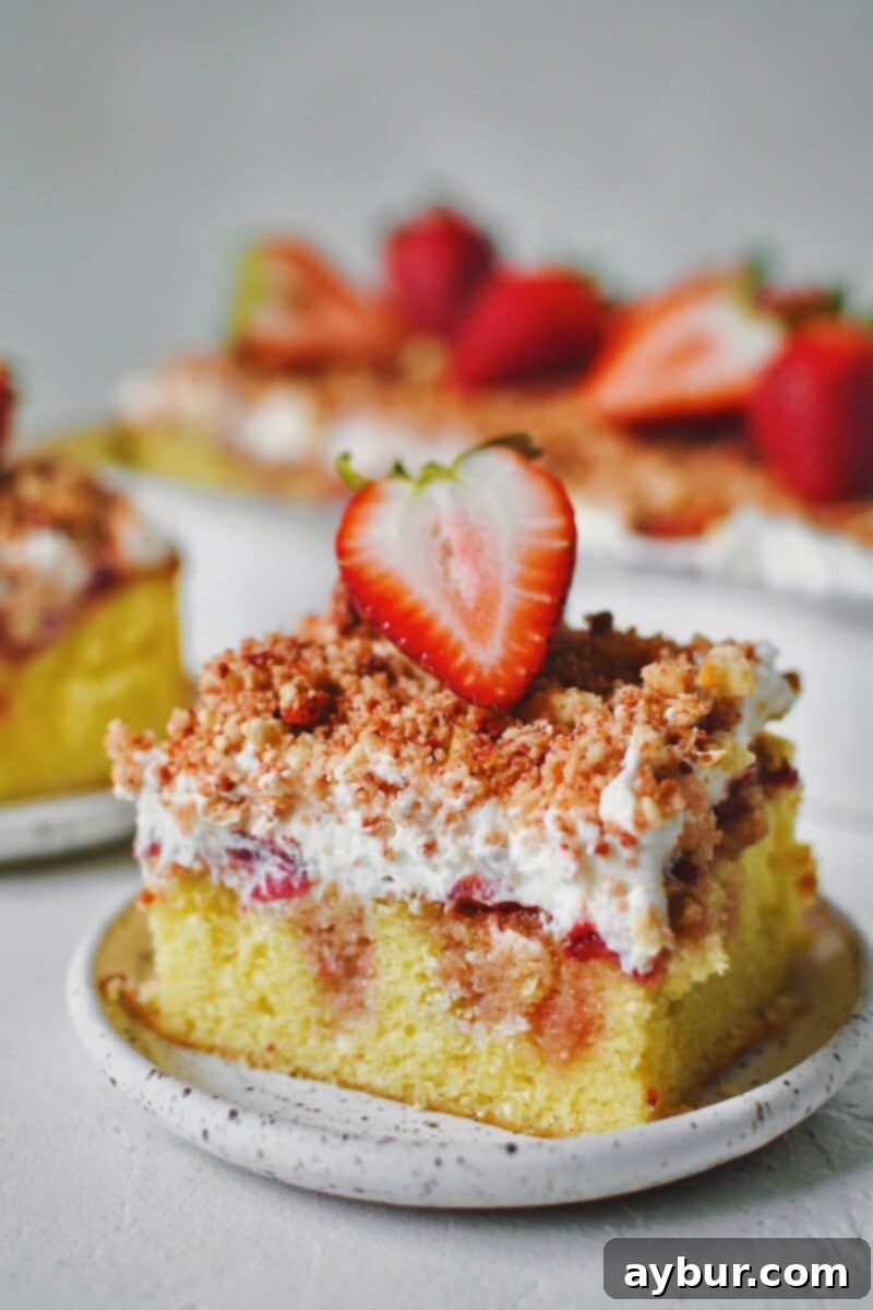 A slice of Strawberry Crunch Cake removed from the pan with a fresh strawberry on top.