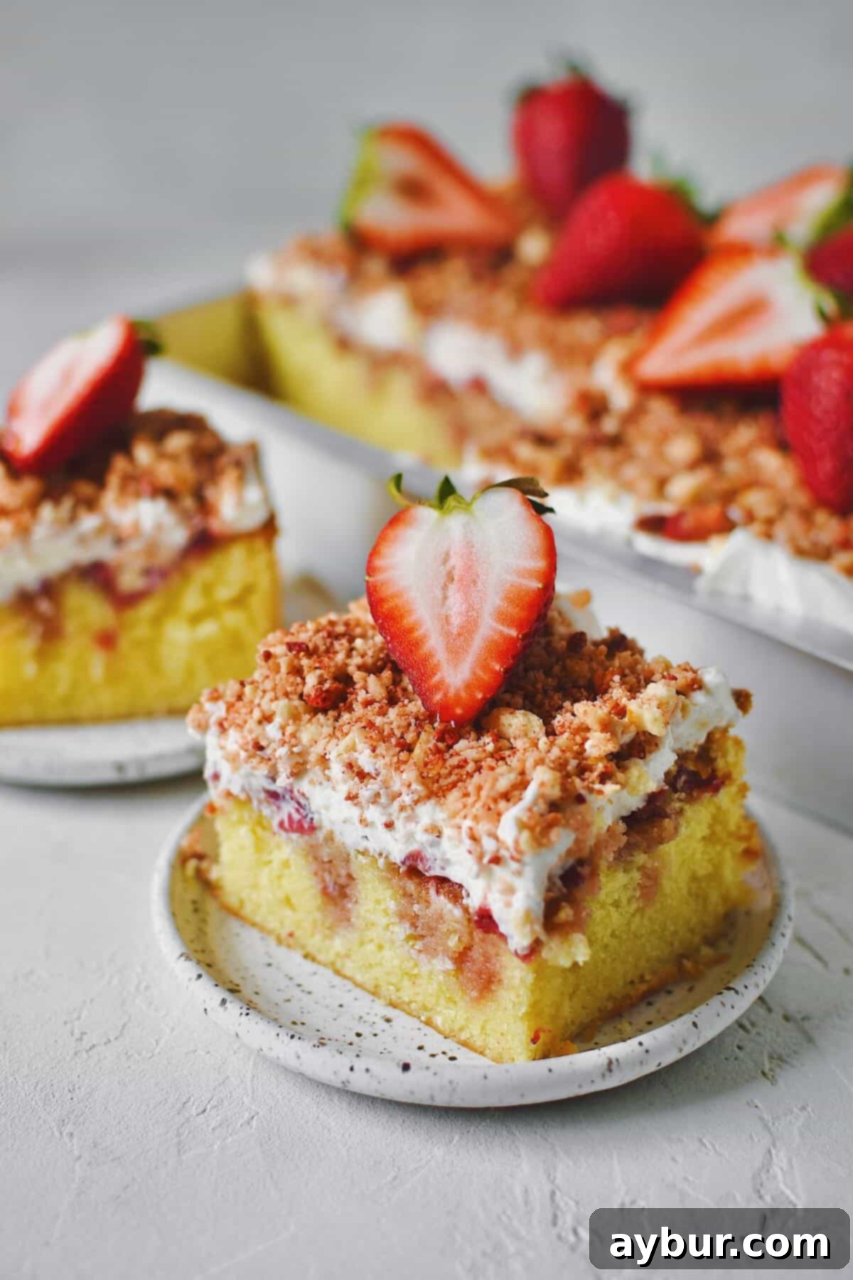 A couple slices of Strawberry Crunch Cake removed from the pan with a fresh strawberry on top.