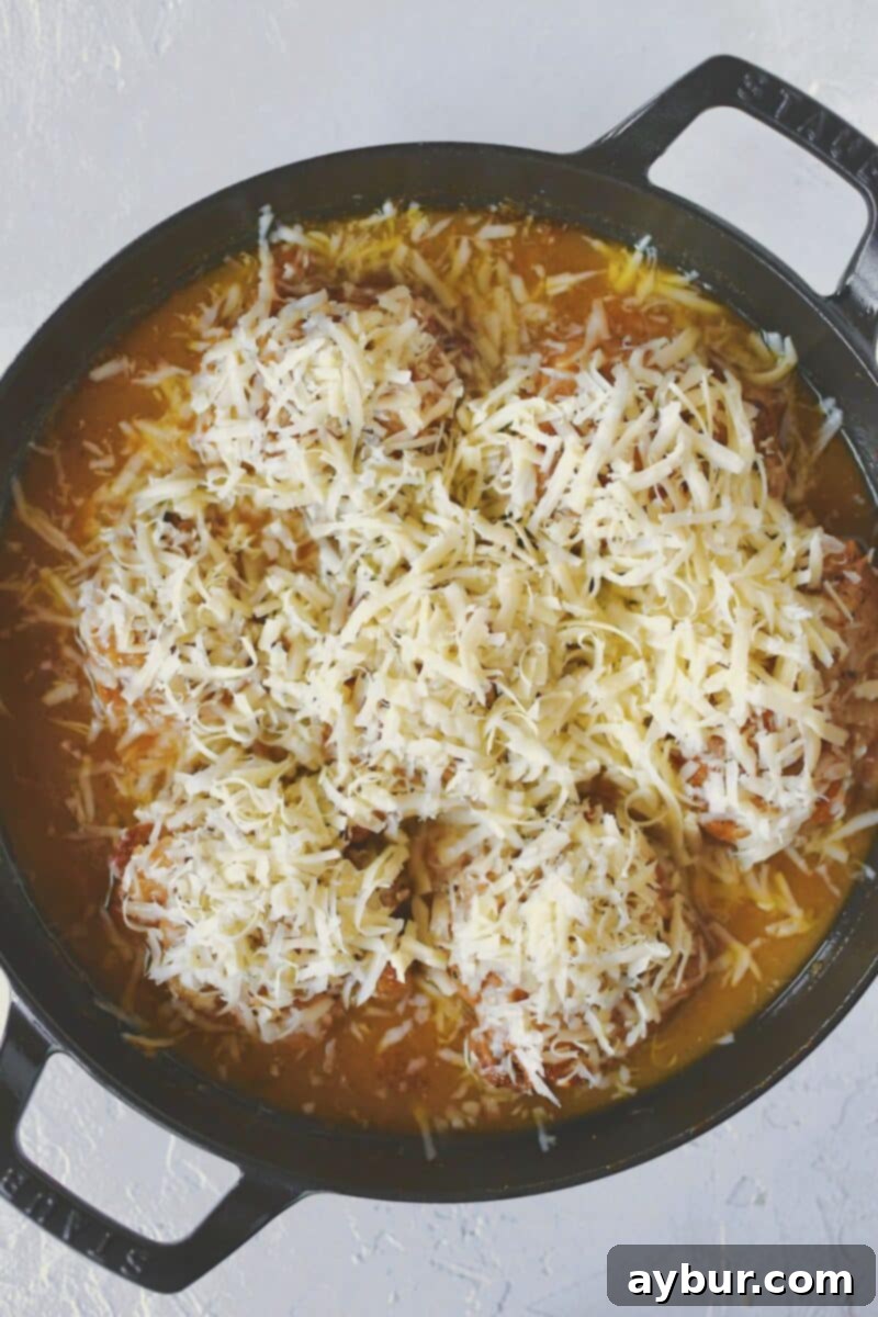 Placing the shredded Gruyère cheese generously on the chicken and onions before broiling.