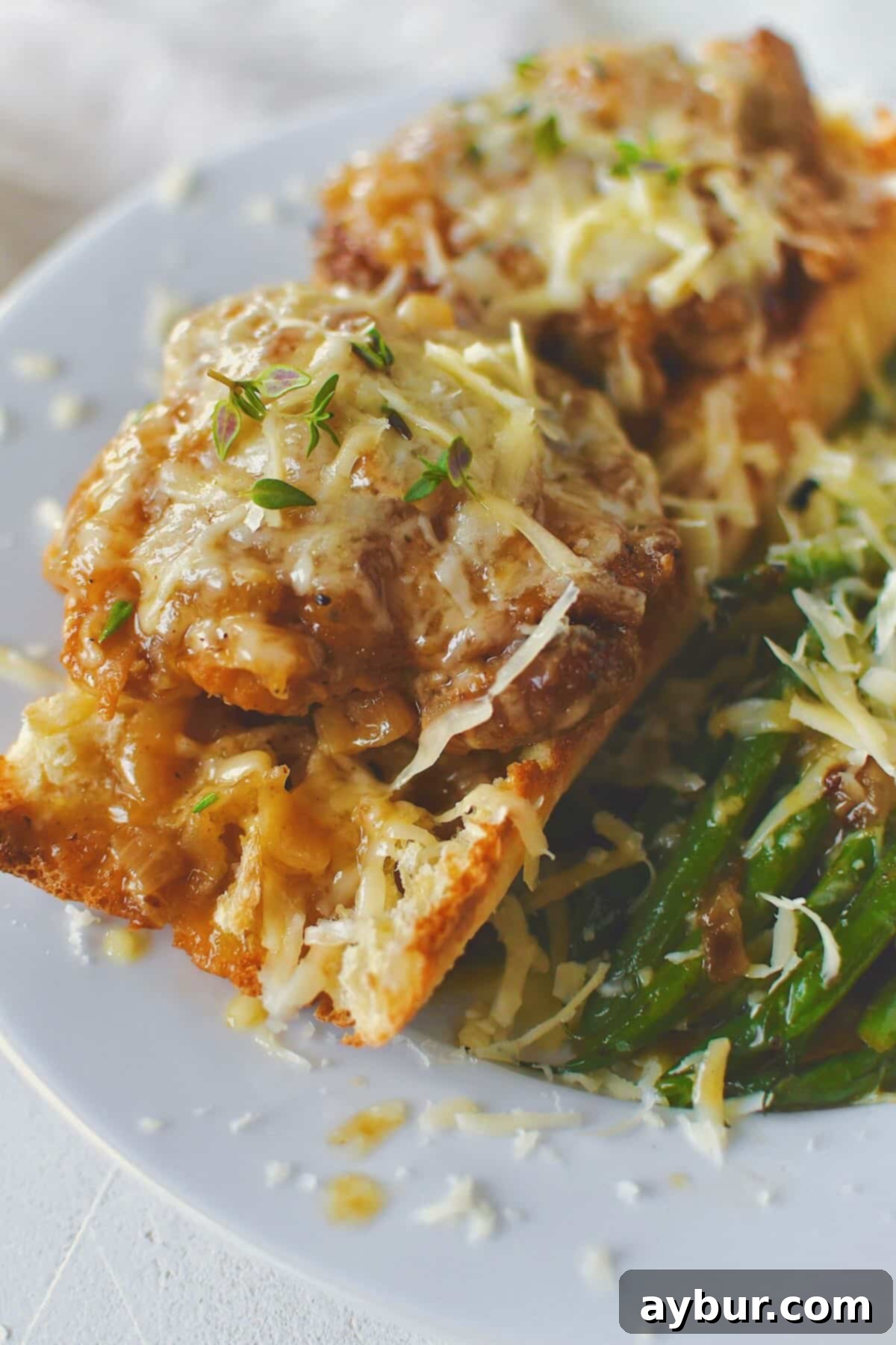 French Onion Chicken served over a piece of crusty bread to soak up the extra sauce and some sauteed green beans, showcasing the deliciousness.