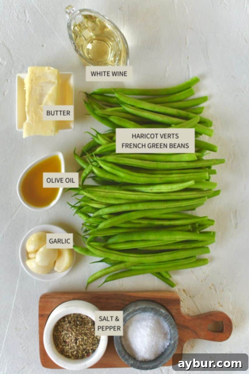 Fresh ingredients laid out on a cutting board, including French haricot verts, garlic, butter, olive oil, salt, pepper, and a bottle of white wine.