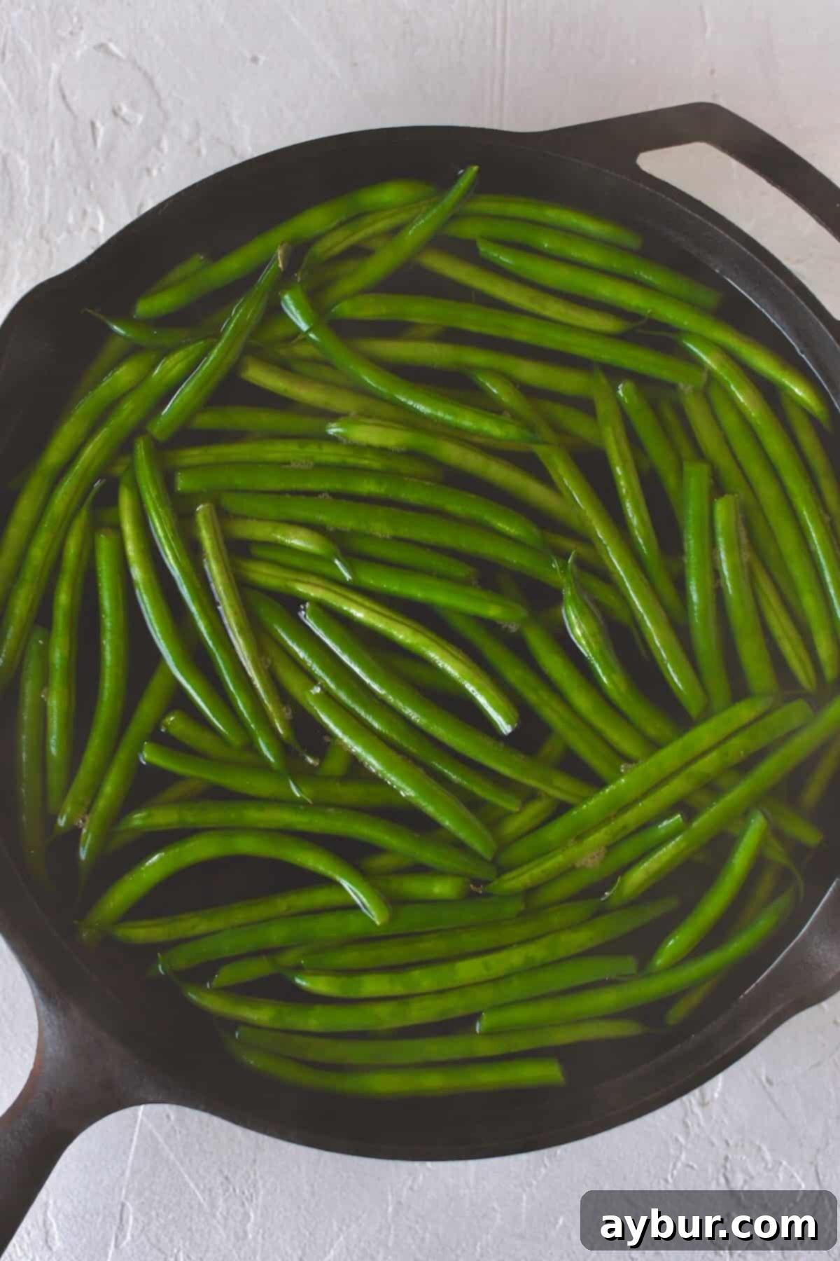 Green beans boiling gently in a large skillet, surrounded by steaming hot water.