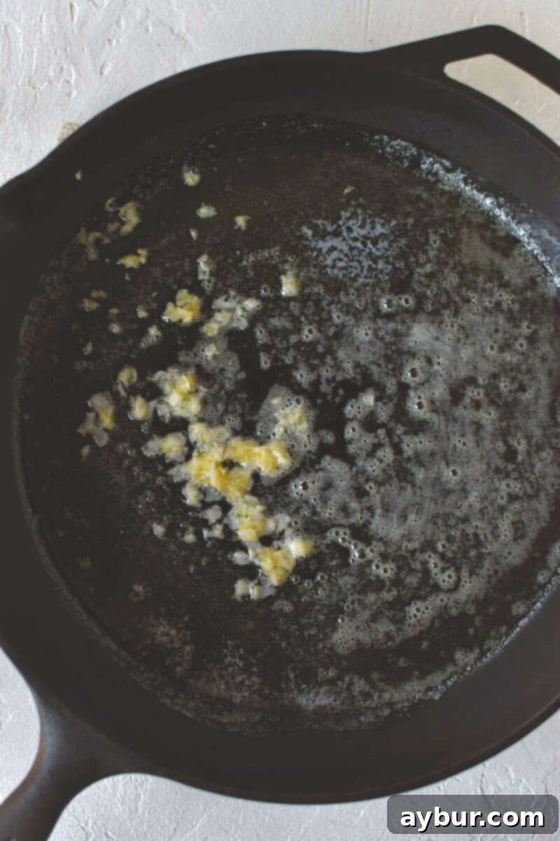 Adding freshly grated garlic to melted butter and olive oil in a hot skillet, creating a fragrant base for the green beans.