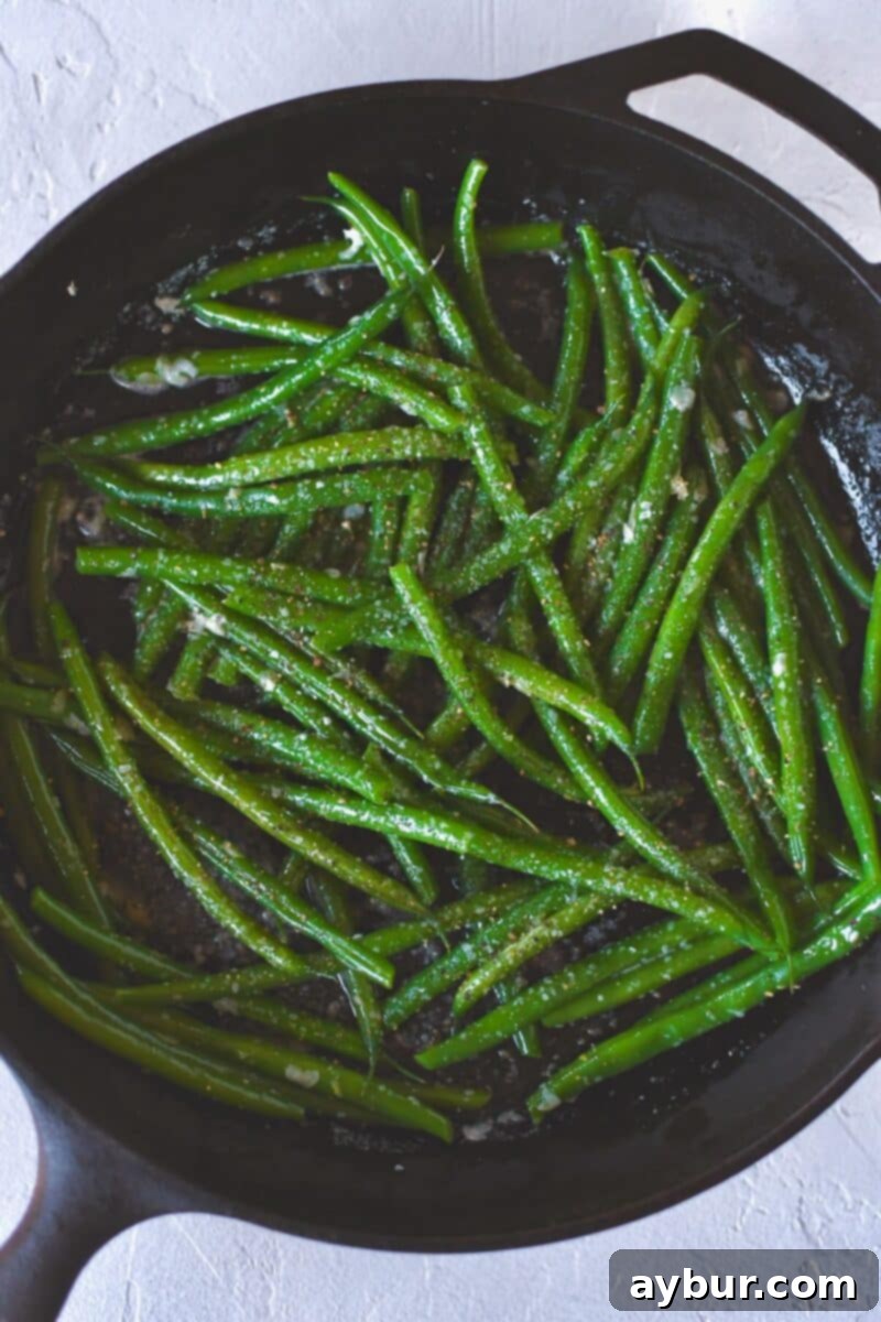 Tossing the green beans in the skillet with the sautéed garlic and butter, preparing to season and deglaze with white wine.