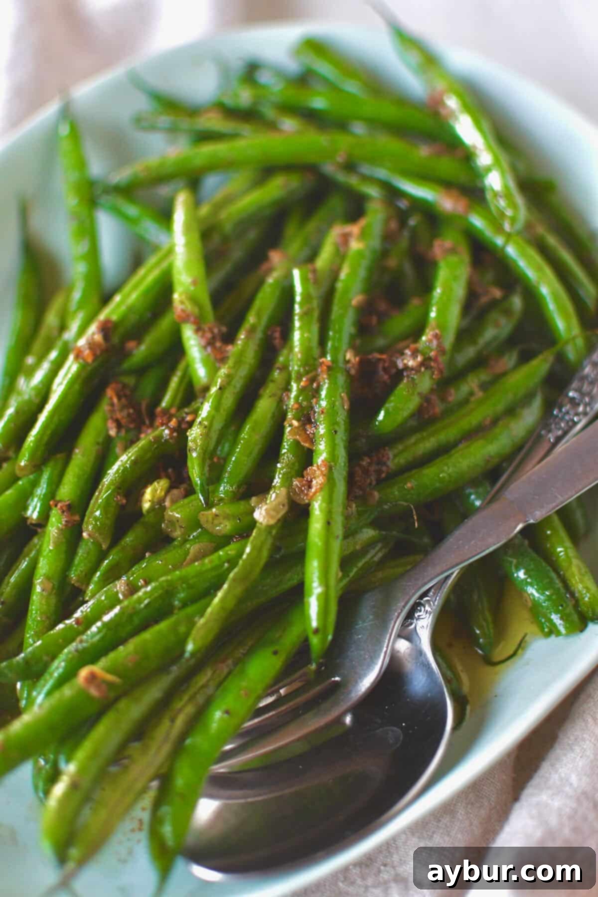A close-up shot of the finished Sautéed Green Beans piled high on a serving dish, generously coated with savory garlic and butter.
