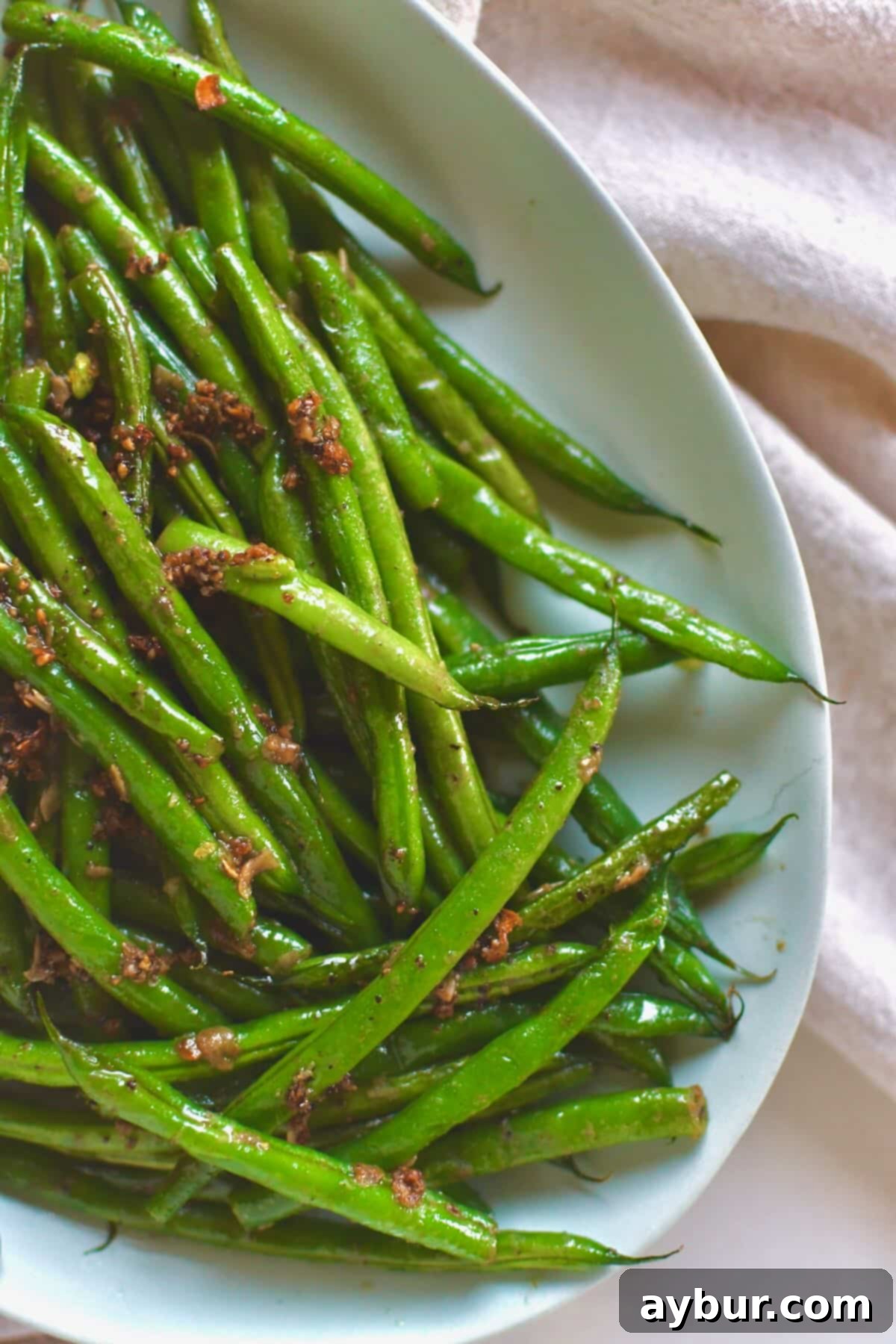 A vibrant platter of Sautéed Green Beans, perfectly cooked with a golden hue from the garlic and butter, ready for serving.