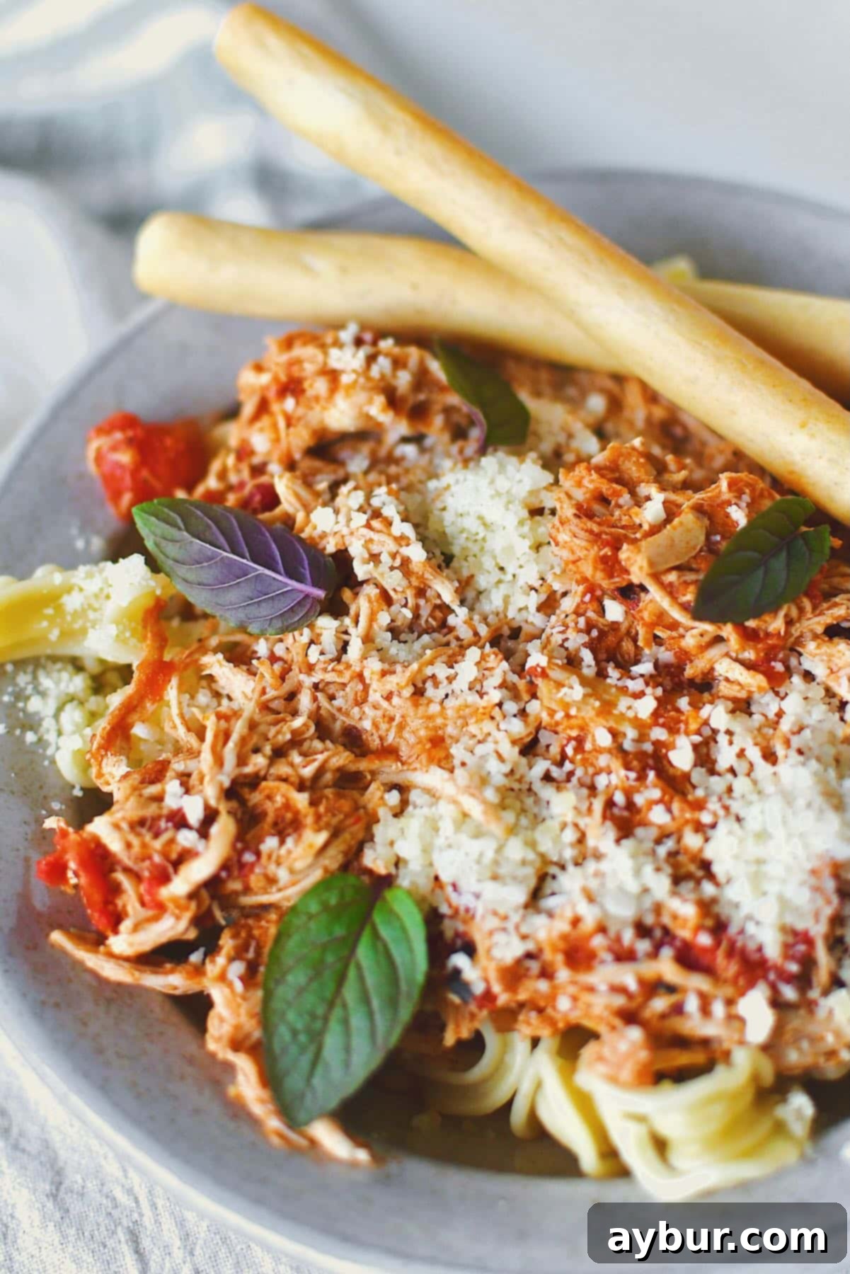 Chicken Marinara served in a bowl over pasta, topped with basil and served with grissini breadstick on the side.