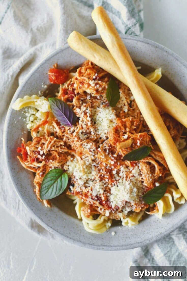 Chicken Marinara served in a bowl over pasta, topped with basil and served with grissini breadstick on the side.