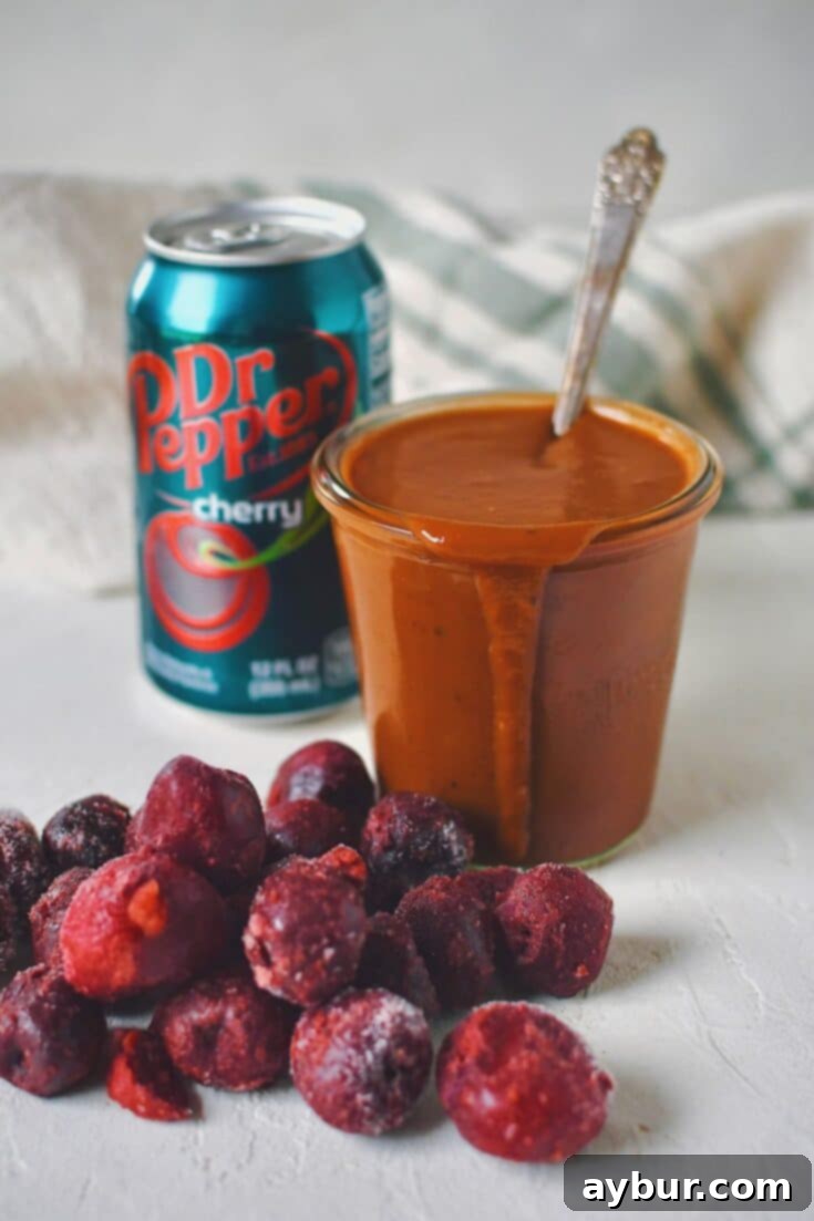 Finished Dr. Pepper BBQ Sauce in a jar that has a spoon in it, with a can of cherry dr. pepper behind it and some frozen cherries in front.