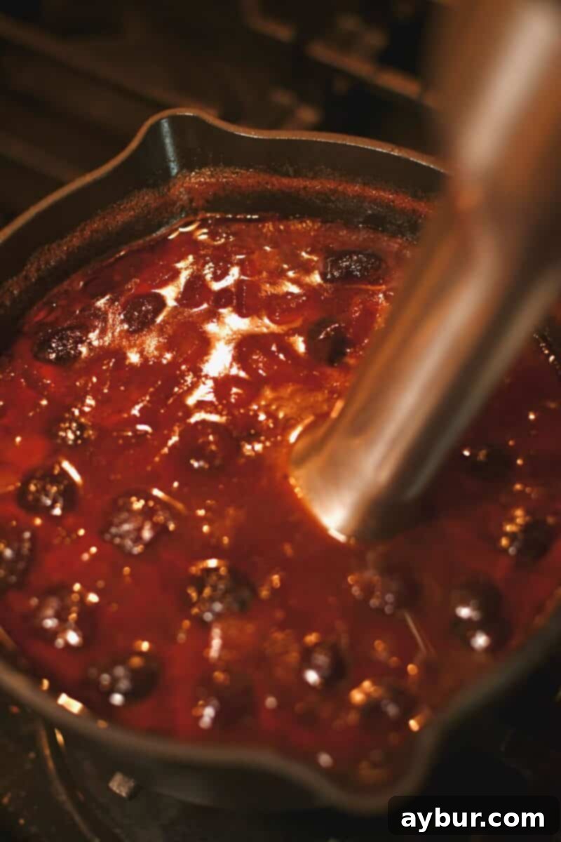 Using an immersion blender to puree the simmering sauce, transforming the cherries, peppers, and onions into a smooth, even consistency.
