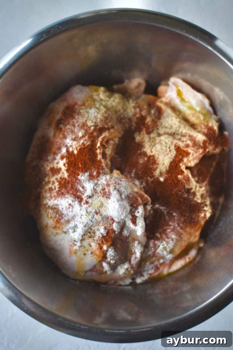 Ultimate Grilled Chicken Thighs 4 Chicken thighs in a bowl with the seasonings tossed over them.