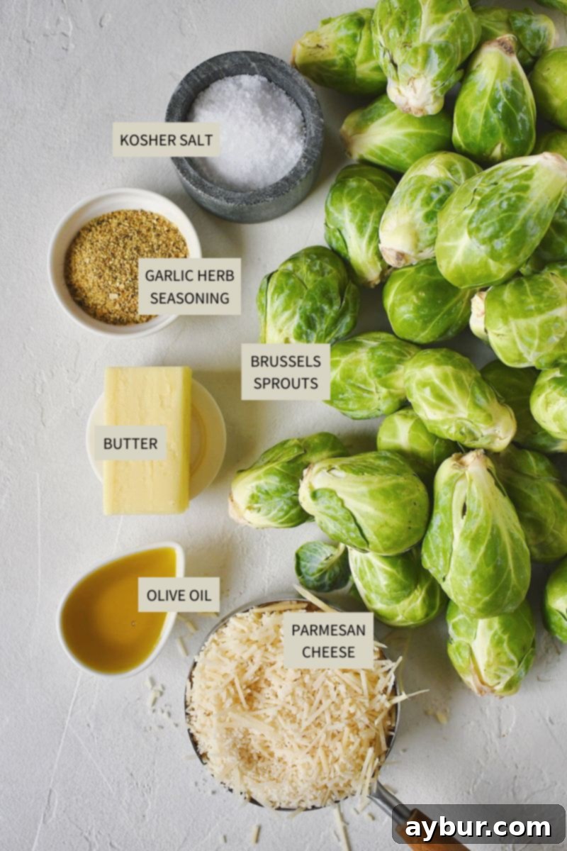 A collection of fresh ingredients laid out: halved Brussels sprouts, olive oil, a shaker of garlic and herb seasoning, kosher salt, unsalted butter, and a bowl of shredded Parmesan cheese.