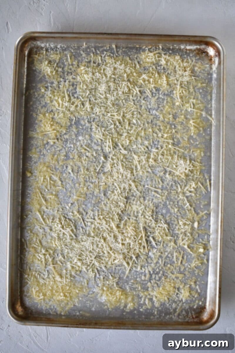 A baking sheet generously dusted with shredded Parmesan cheese over melted butter, forming an even layer.