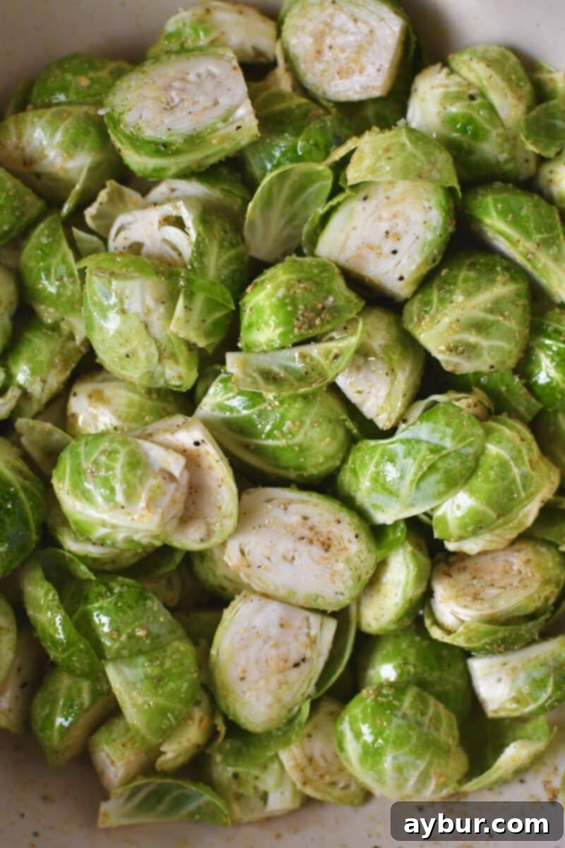 Halved Brussels sprouts thoroughly tossed in a bowl with olive oil and seasoning, ready for roasting.