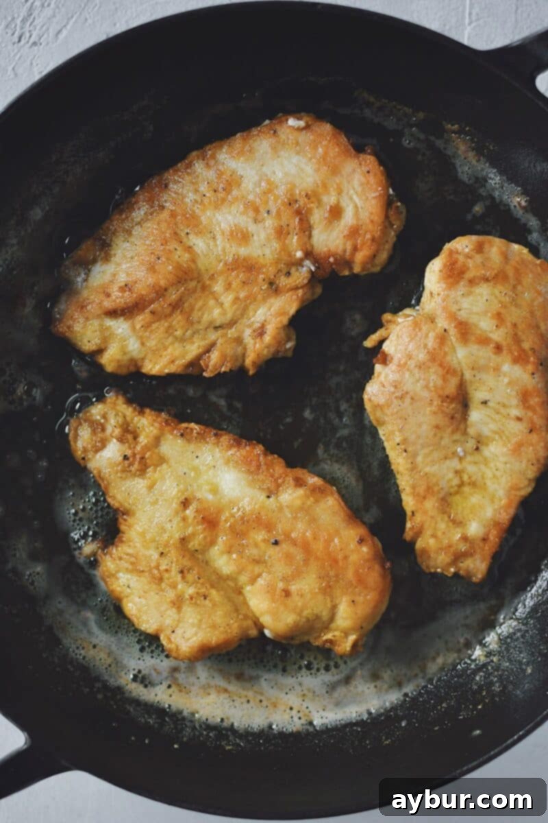 Velvety Mushroom Chicken 5 Golden-brown, dredged chicken pieces sizzling in a hot skillet with olive oil, developing a delicious crust.