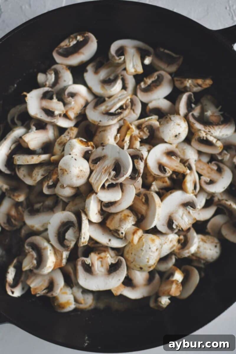 Velvety Mushroom Chicken 6 Freshly sliced button mushrooms being added to the hot skillet after the chicken has been removed, ready to be sautéed.