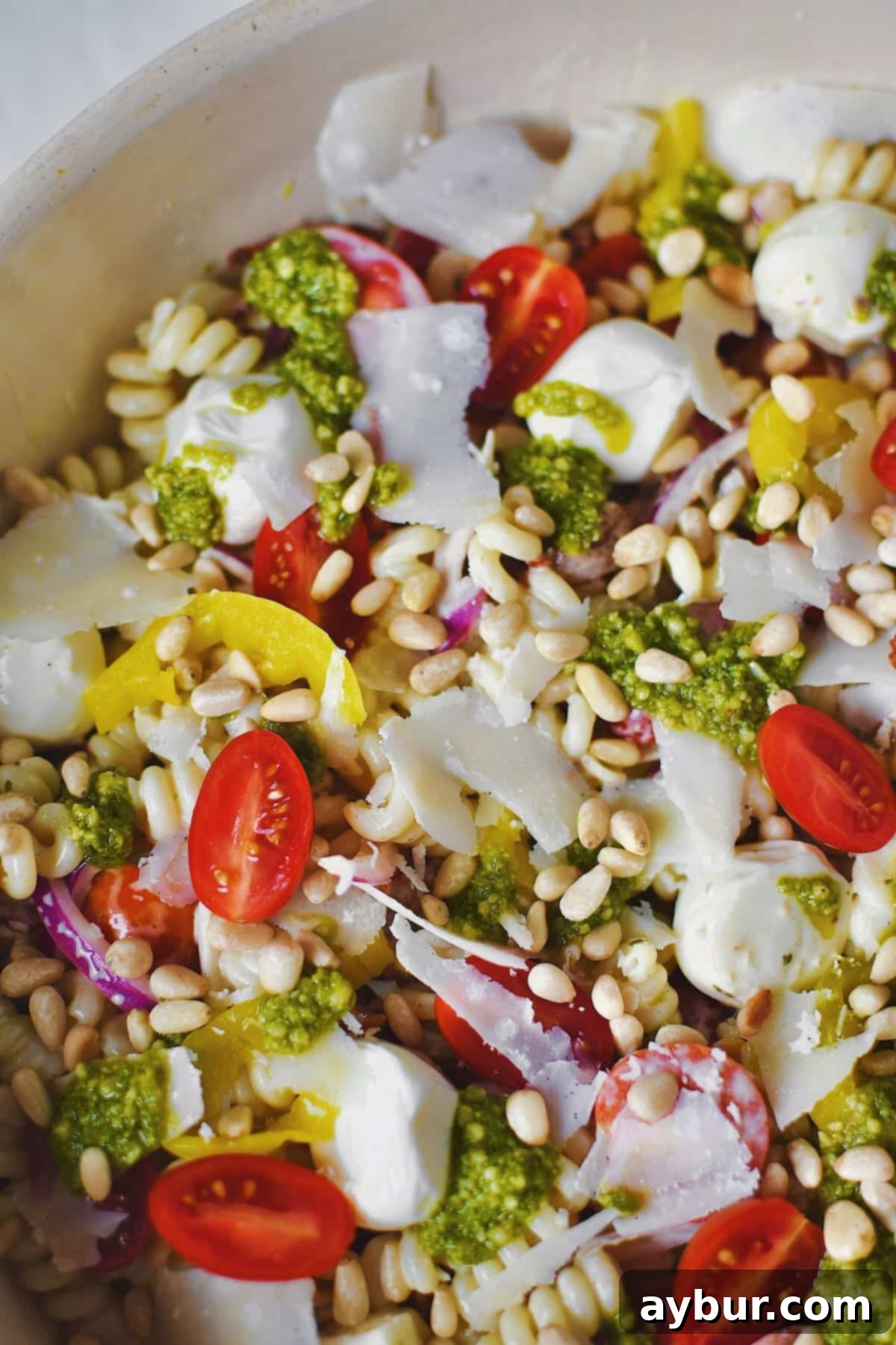 Fully dressed Pesto Pasta Salad topped with pesto and freshly shaved parmesan before serving, showcasing vibrant green pesto, red tomatoes, and white mozzarella against the pasta.