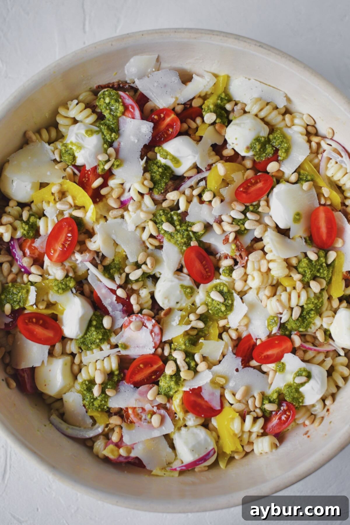 Close-up of the fully dressed Pesto Pasta Salad, garnished with fresh pesto dollops, shaved Parmesan, and pine nuts, ready for serving.