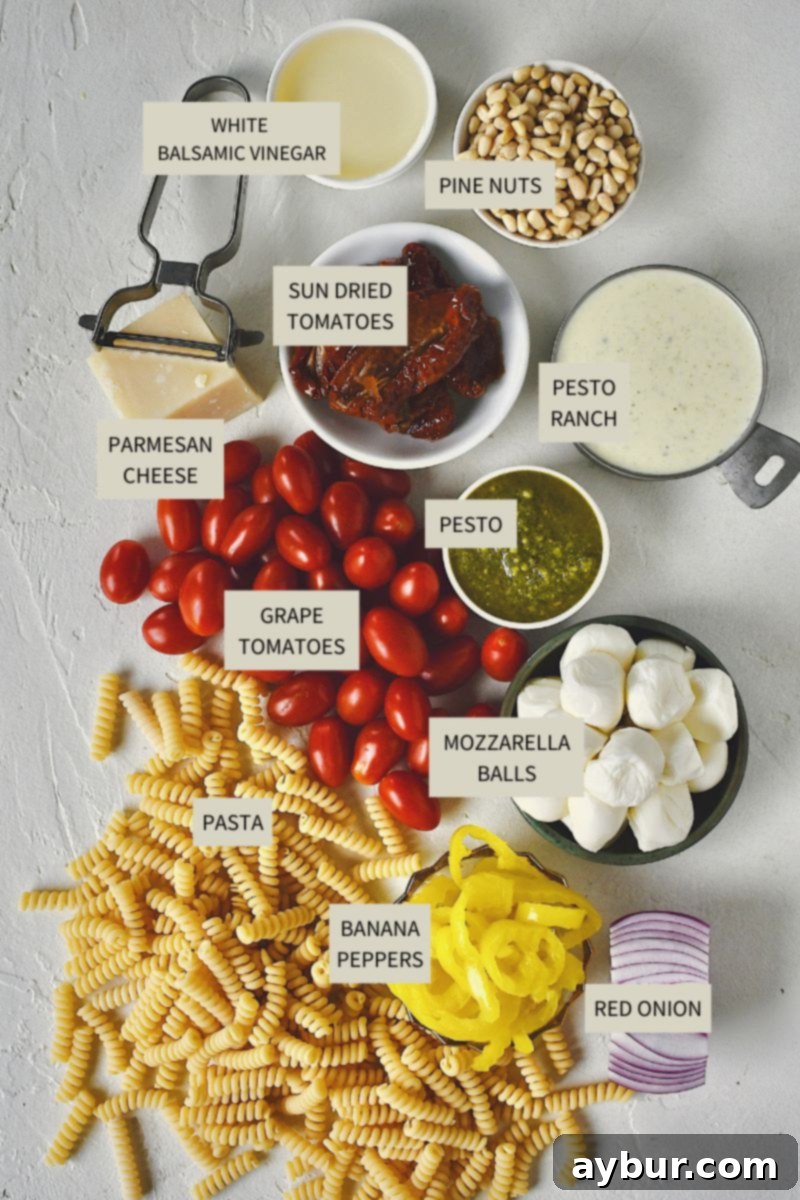 Ingredients needed to make Pesto Pasta Salad laid out on a wooden cutting board, including pasta, tomatoes, mozzarella, pine nuts, and dressing components.